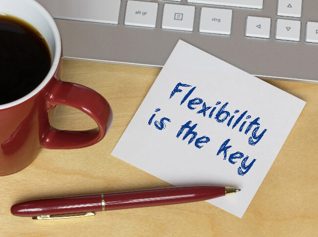Adaptability and Growth: desk with coffee, laptop, pen and a post-it with the words "flexibility is the key"