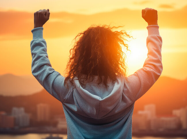 a person facing the sunset with their arms up.