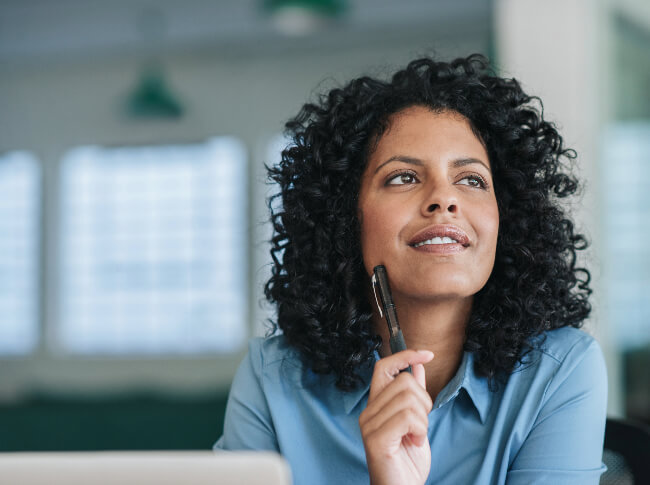 Woman with pen in her hand against her face staring in wonderment.