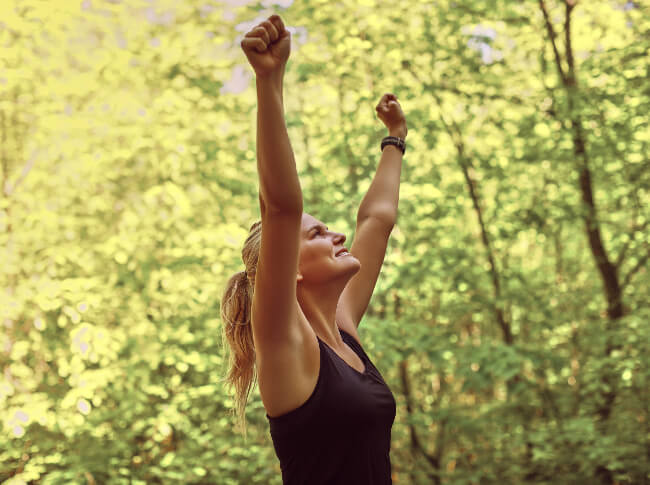 Woman in the woods with arms raised up.