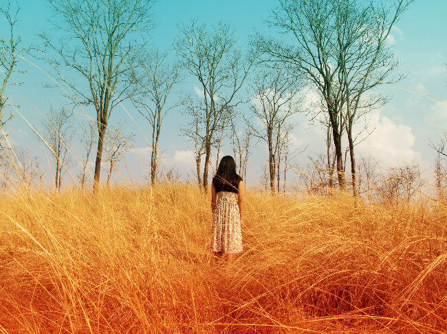 Womn in a field with back to camera looking t the skky.