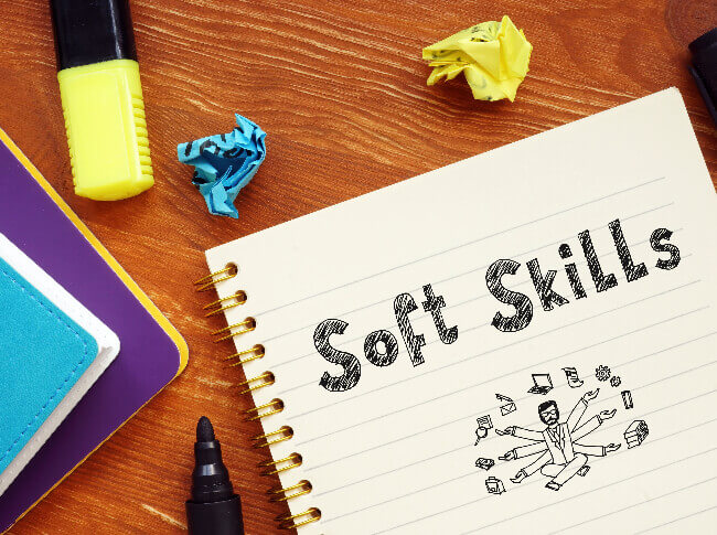 Spiral writing notebook with Soft Skills and a drawing on it.  The notebook is on a surface that also have a pen some other books, highlighters and crumpled papers