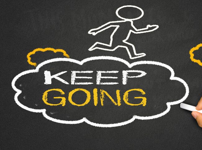 a chalk illustraiting of a stick figure running over a cloud  tht says KEEP GOING on a blackboard backdrop