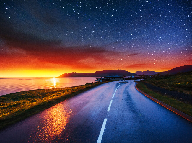 A picture of a beautiful evening showing a road, water and mountains