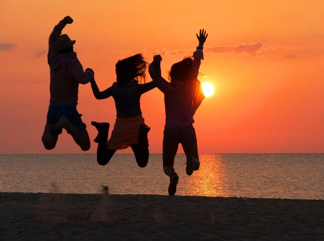 Three  people jumping with the water and sunset in the background
