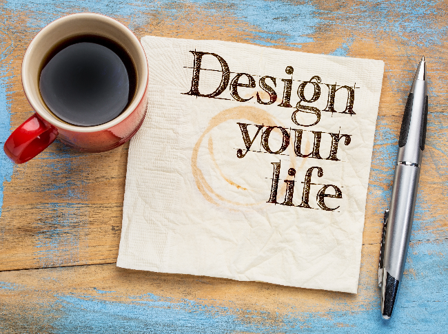 A cup of coffee, a napkin that says "design your life", and a pen.