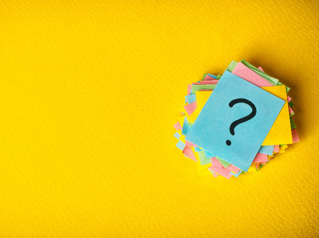 picture of a stack of multi-colored post it notes with the top post-it with a question mark on a yellow background