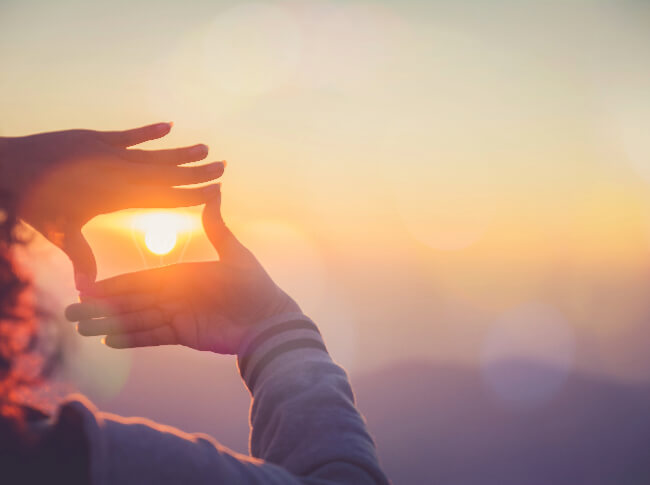 someone's hands in a rectangle shape framing the sun. 